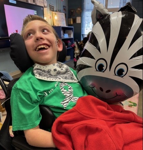 A smiling boy in a wheelchair holds and zebra balloon.