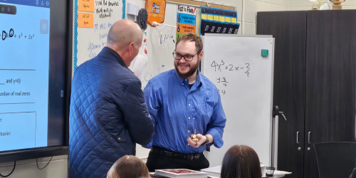 Teacher shaking hands with man in classroom.
