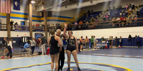 Girl wrestler with hand raised by ref with opponent in gym with fans. 