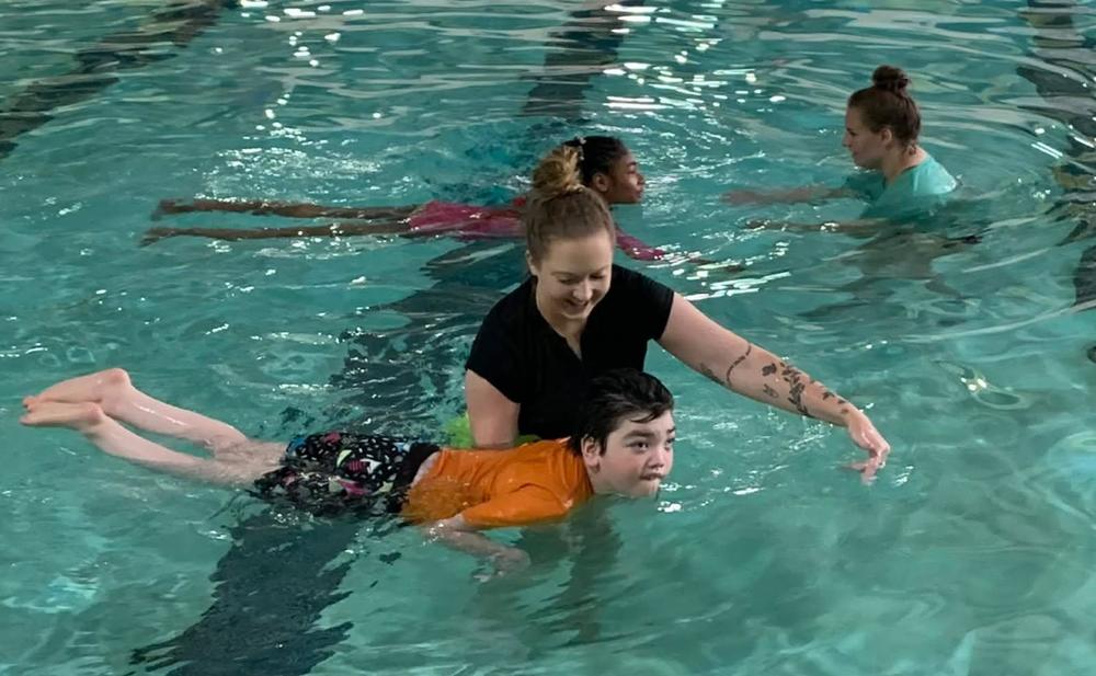 Two adults help two children practice in a swimming pool.