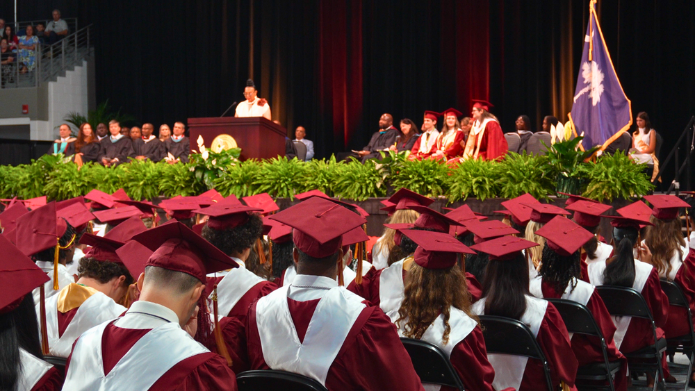 South Aiken High School graduates sitting in their cap and gowns listening to a speaker at graduation.