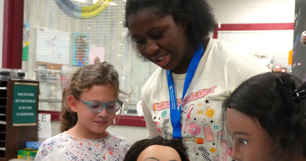 Two students practice cosmetology and hair care on a mannequin.