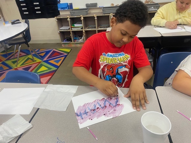 A boy is rubbing a blackberry over a sheet of paper with the word math written on it.