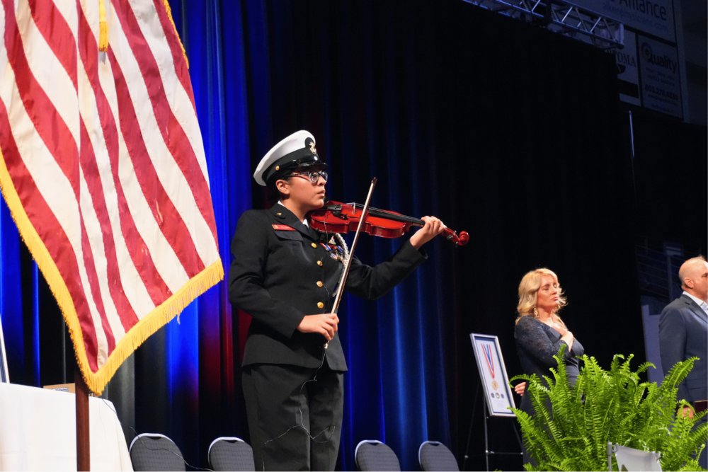 A junior cadet standing on a stage playing a violin.
