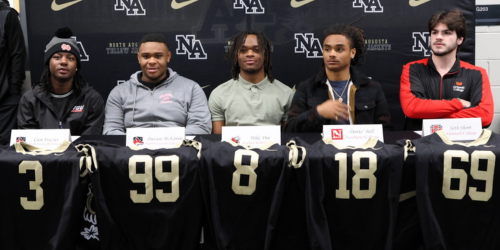 5 Players sitting with football jerseys and name placards.