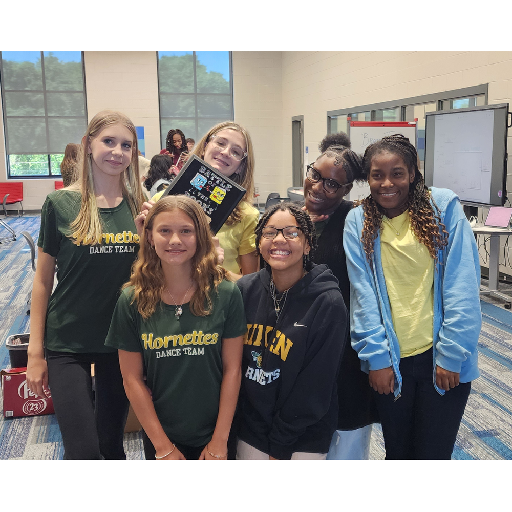 Six girls smiling and holding a plaque. 