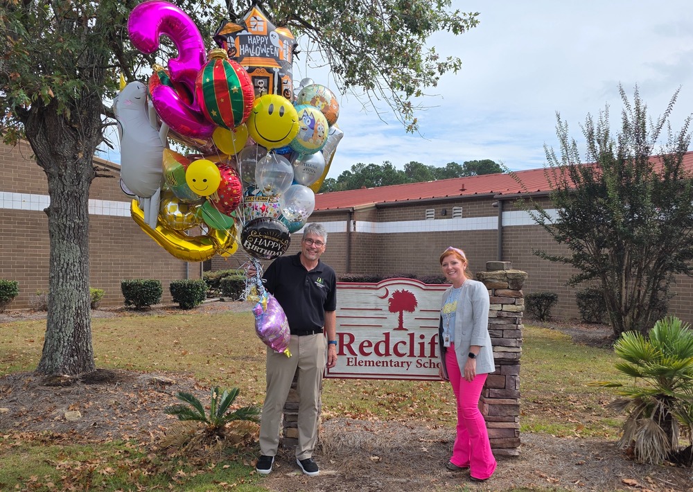 Two people standing by Redcliffe sign with big bunch of balloons.