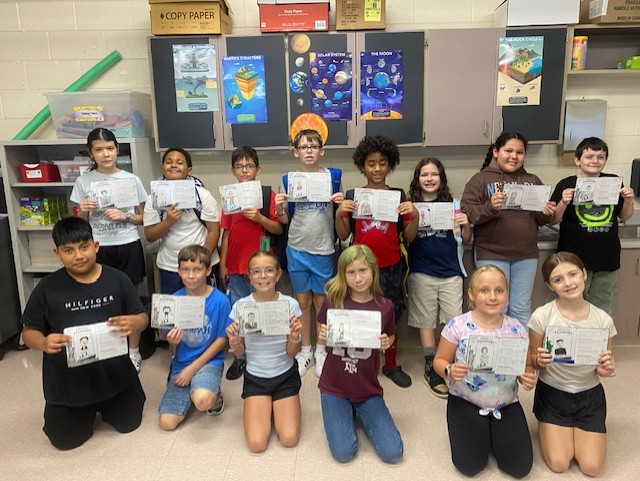 A class of students standing in two rows holding up pieces of paper.