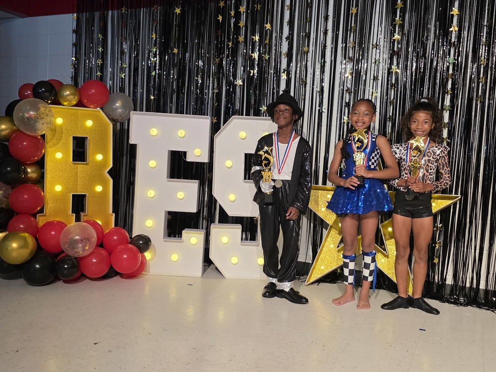 Winners of talent show standing with trophies next to RES sign.