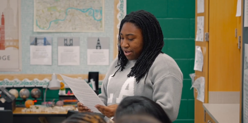 Student standing in front of a class reading.