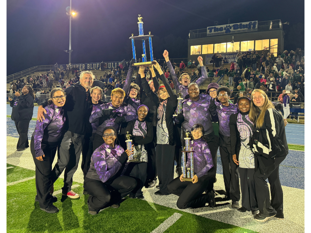Students in band uniforms smiling and holding trophies