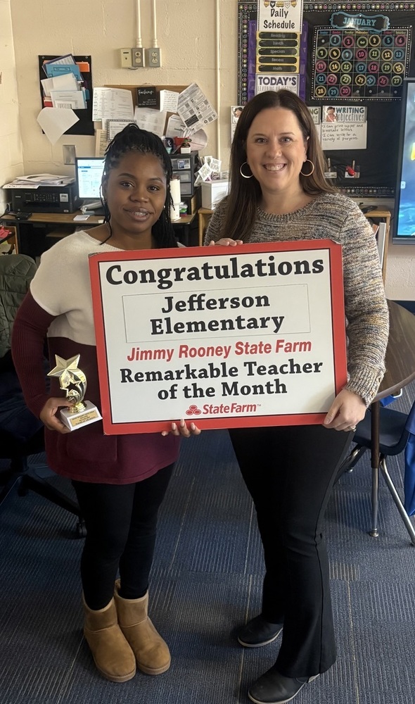 Two women hold a sign for Teacher of the Month.