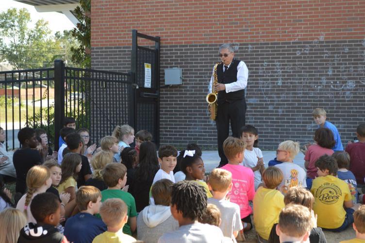 Substitute Teacher playing saxophone for fifth grade students outside school. 