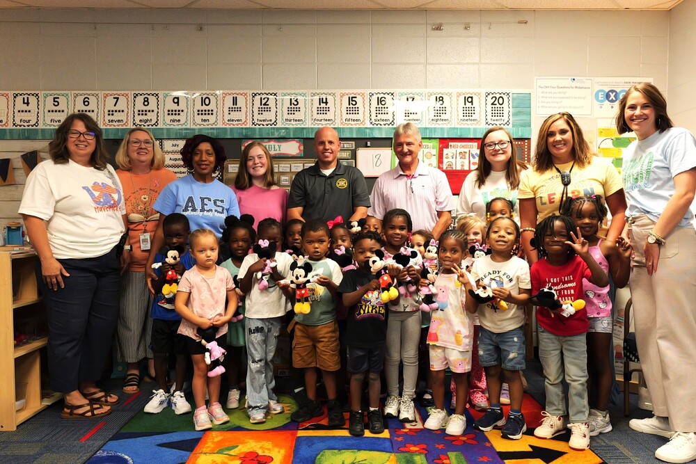 Students posing with teachers and Aiken County Public Safety Officers holding stuffed animals.
