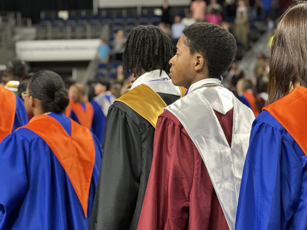Image from the back of students in graduation robes.