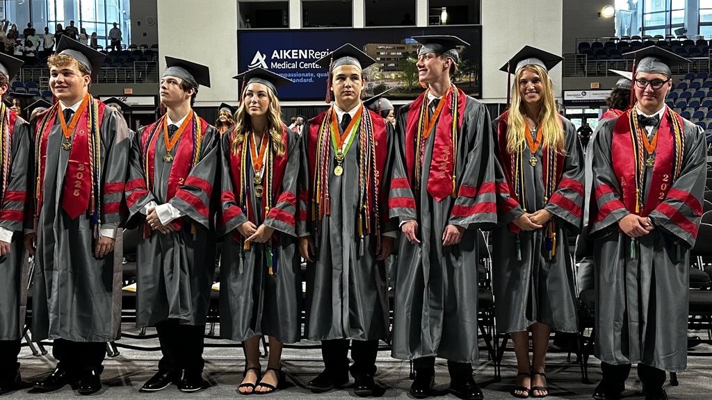 Three male and one female group of graduates in gray and burgundy robes and caps.