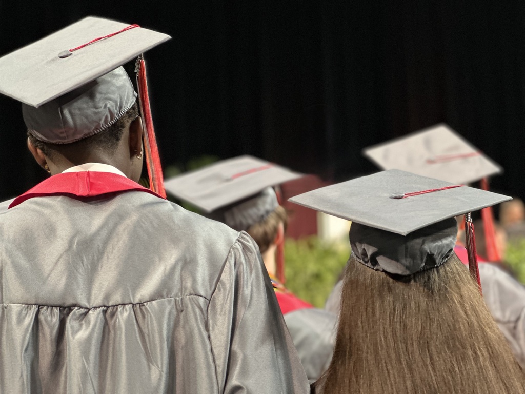 The back of graduates heads with gray and burgundy cap and gowns.