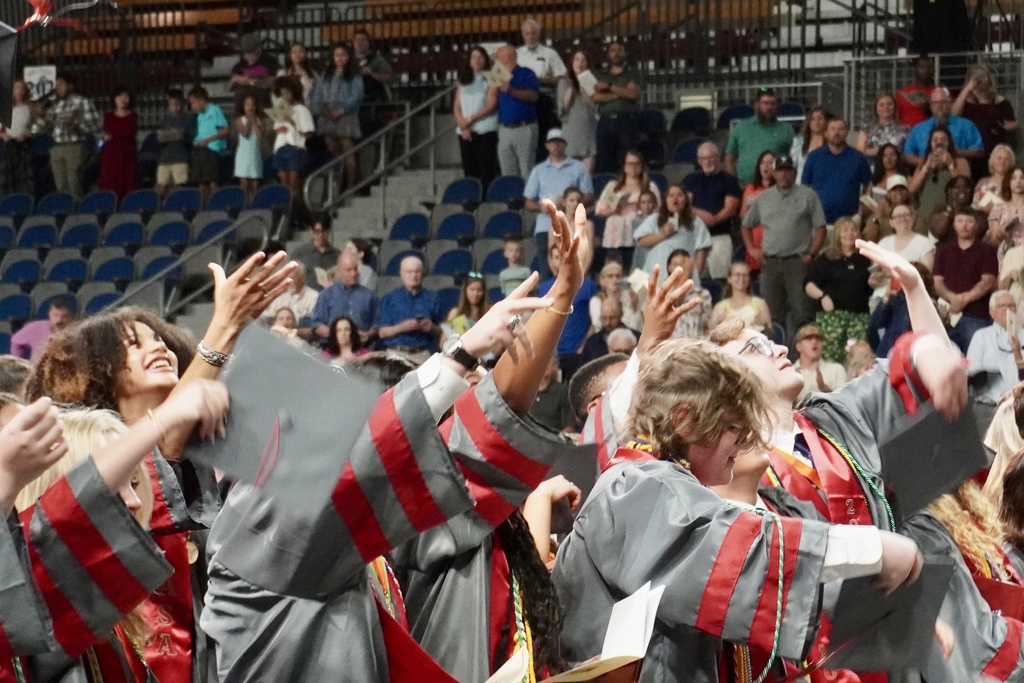 Students in Gray and Burgundy graduation robes throwing up caps.