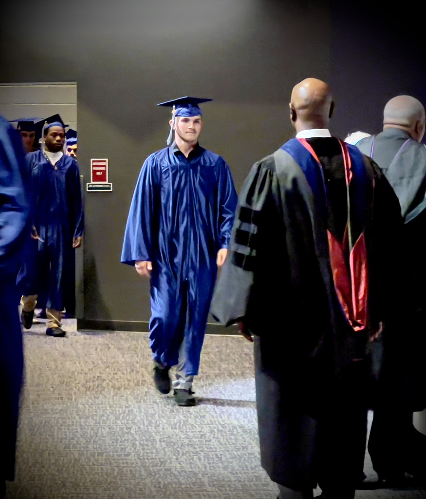 Male Adult Graduate in a blue cap and gown walking.