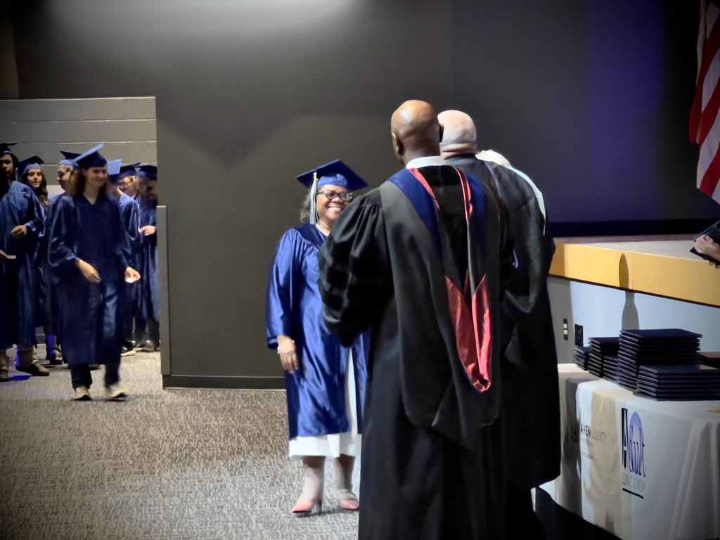 A female adult education graduate in a blue robe and cap smiling.