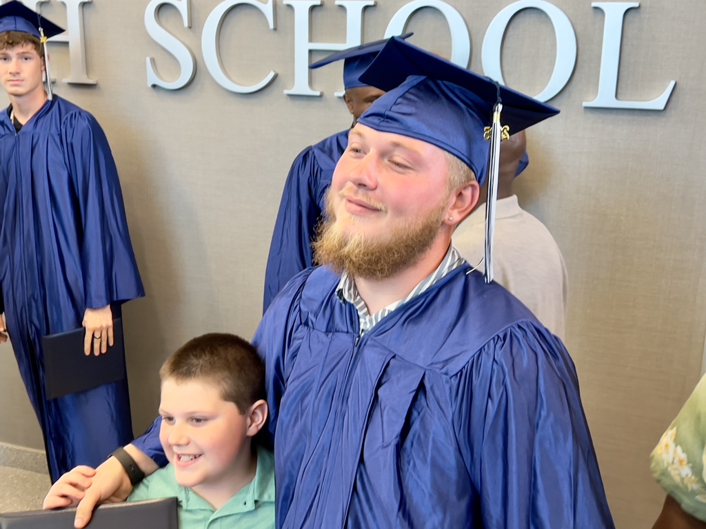 Male Adult Education Graduate in a blue cap and gown with his arm around a young boy.