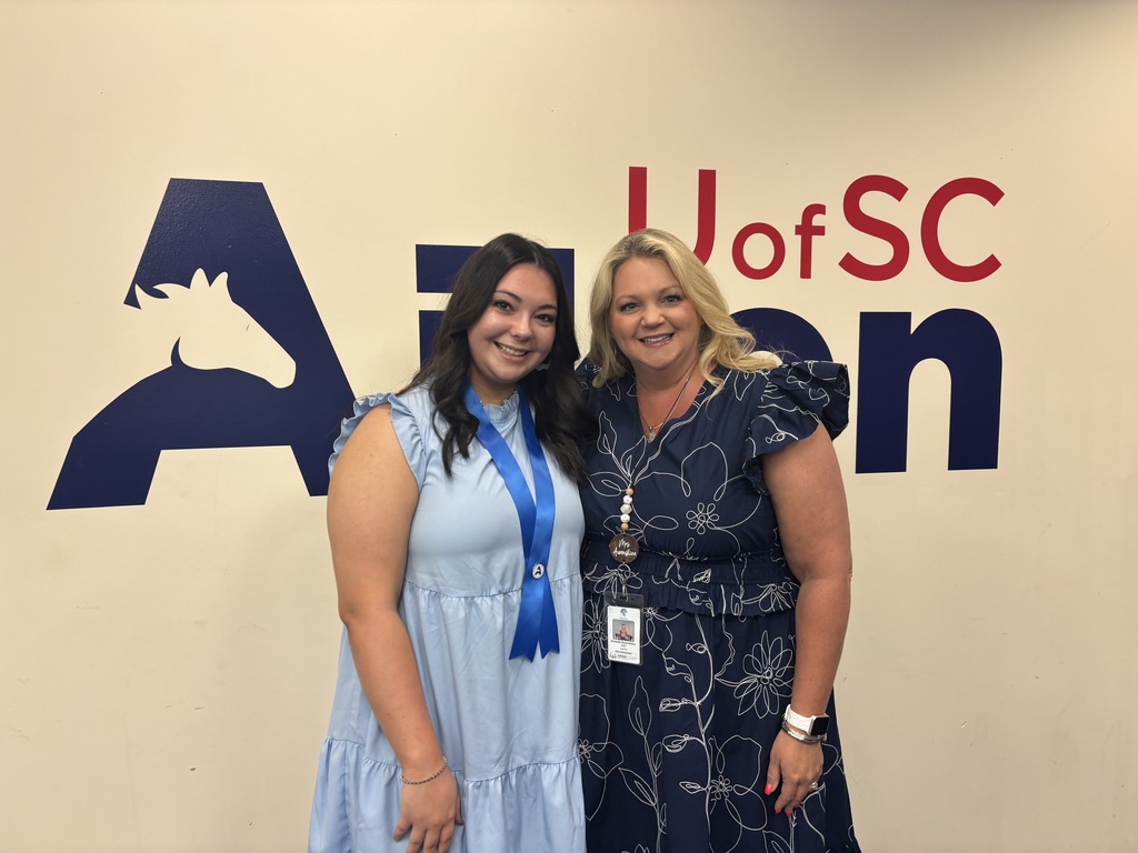 2 Teachers in dresses in front of a USCA mural.