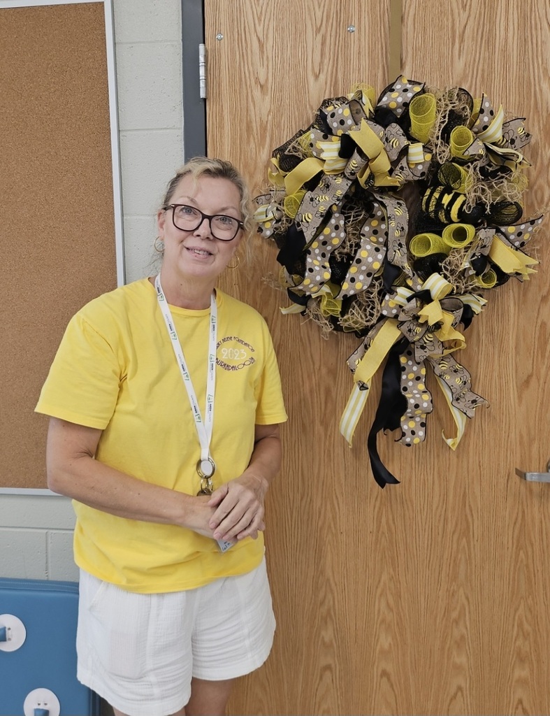 Teacher standing in front of door with yellow and black jacket wreath. 