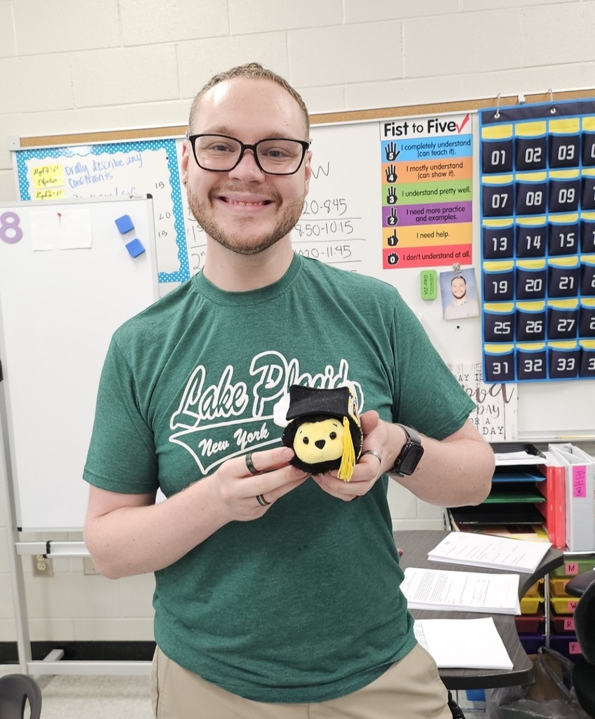 Dr. Ball holding a stuffed bee with grad cap in classroom.