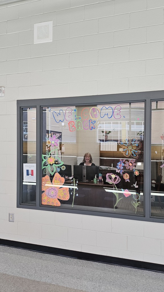 Colorful Welcome Back to School with flowers and teacher smiling behind glass. 
