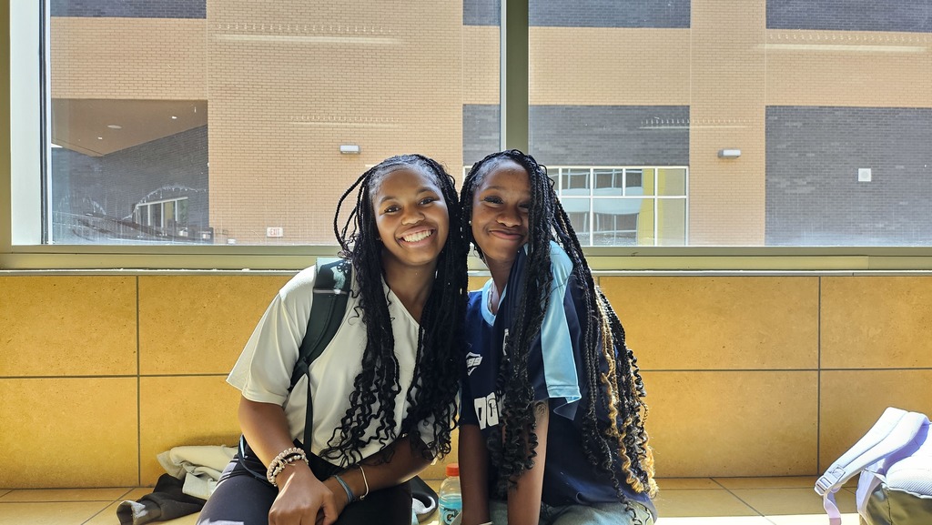 2 girls smiling sitting on ledge. 