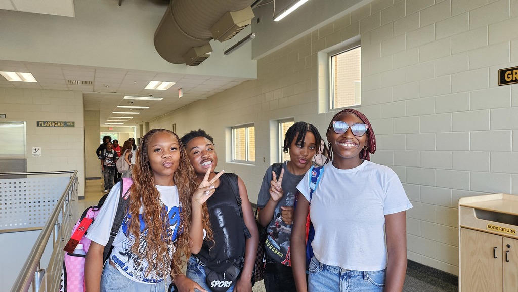 4 Students standing in hallway giving peace symbol.