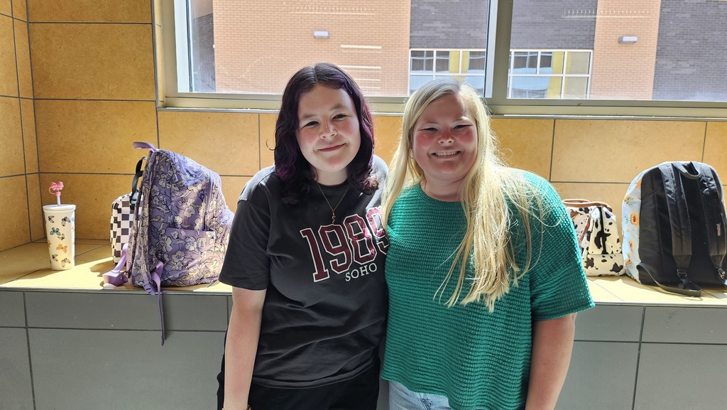 2 Girls smiling with backpacks and sun beaming through window. 