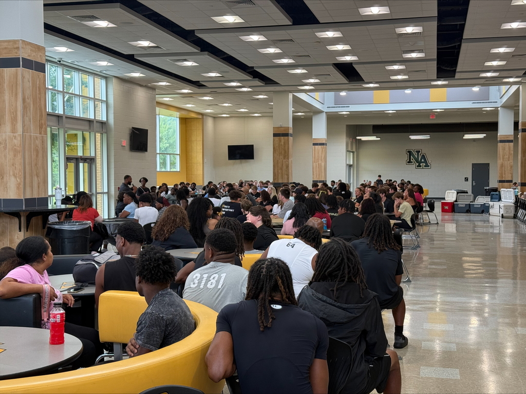 Group picture of moms and son football players having breakfast in cafeteria.