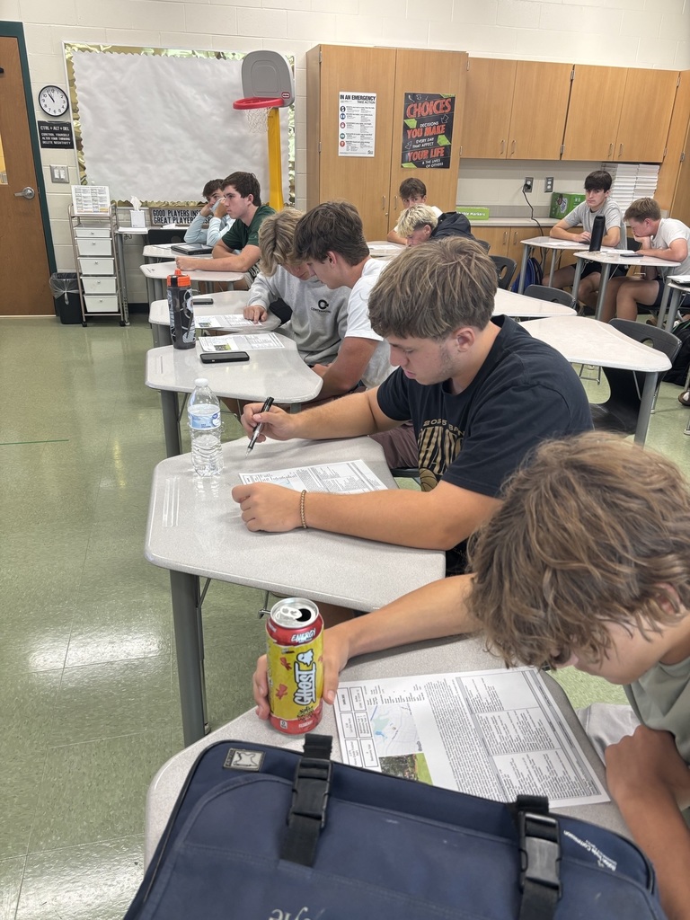 A row of students at their desks reading a sheet of paper.