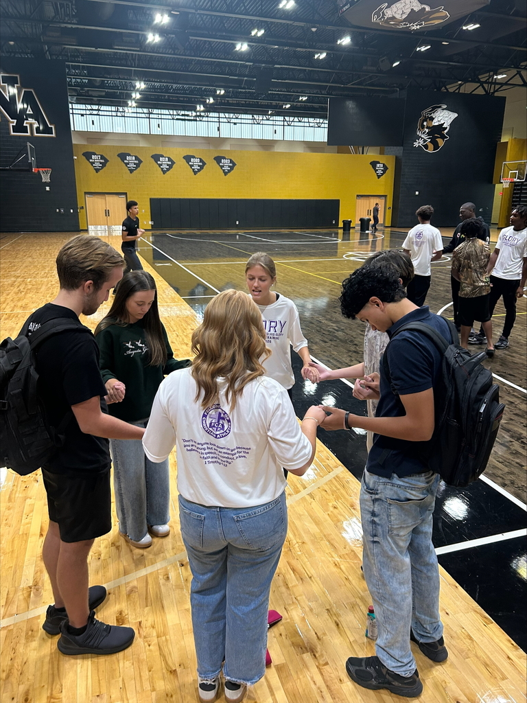 6 Students holding hands praying in a gym. 