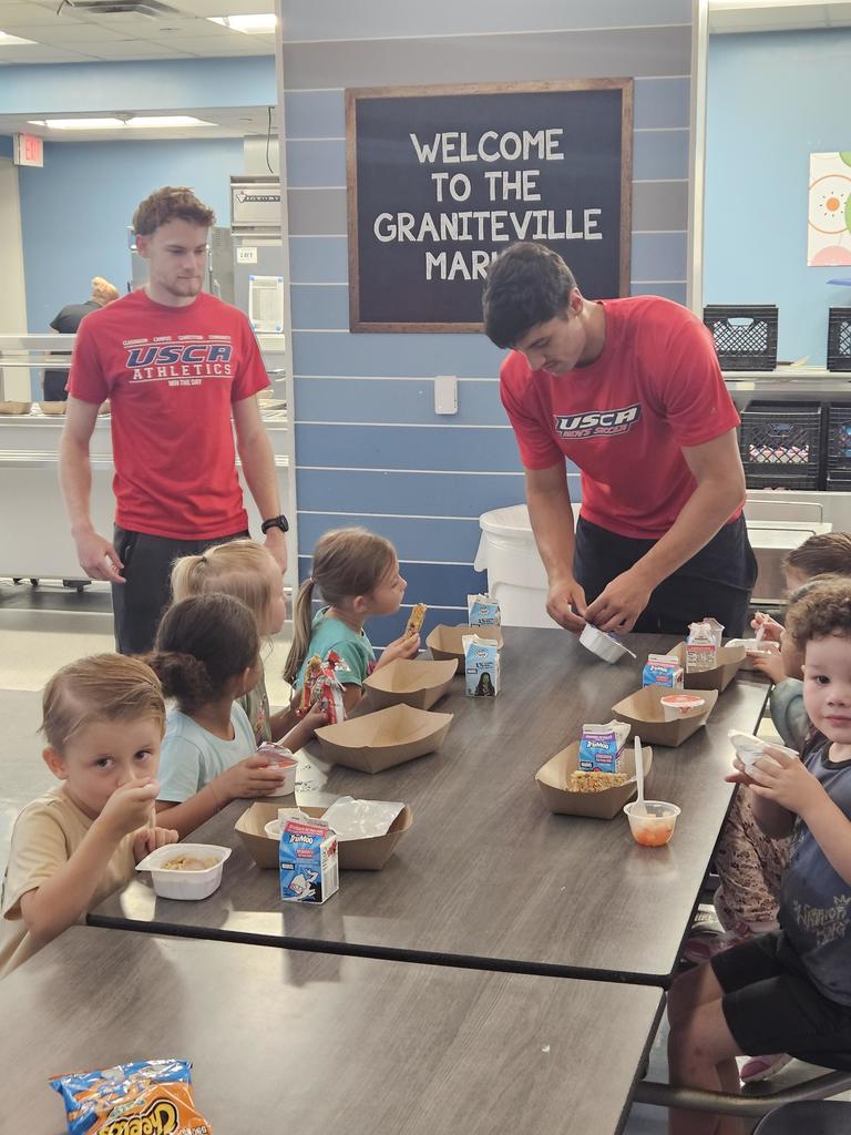 2 young men helping school children in a school cafeteria