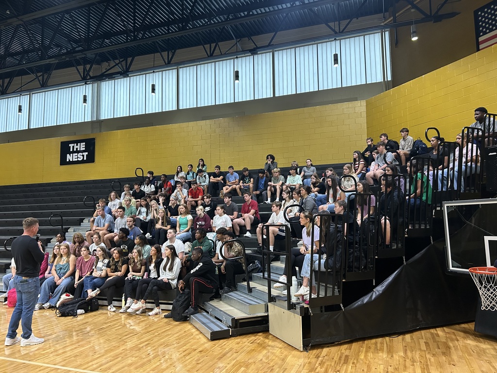 Group of students sitting in gym listening to guest speaker. 