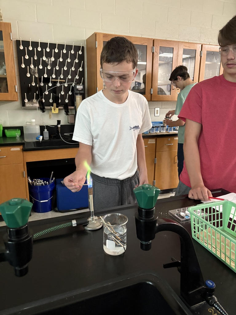 2 students working in science lab with flame and goggles.