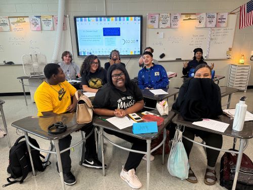 Group of students sitting at desks smiling at camera.