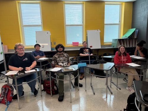 Group of students sitting at desks smiling at camera.