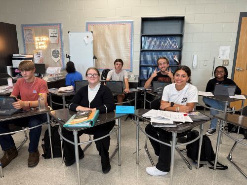 Group of students sitting at desks smiling at camera.