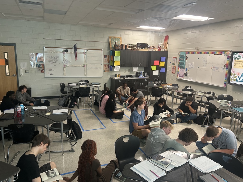 Students sitting on floor of classroom taking notes.