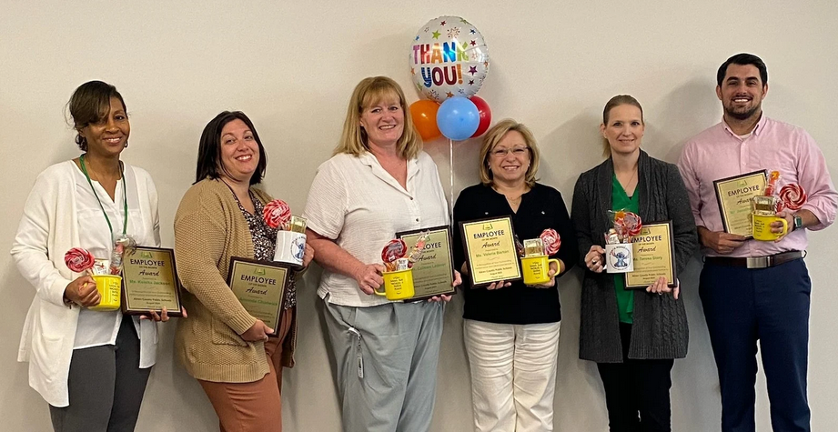 6 people holding plaques and smiling with mugs of sweets and balloons. 