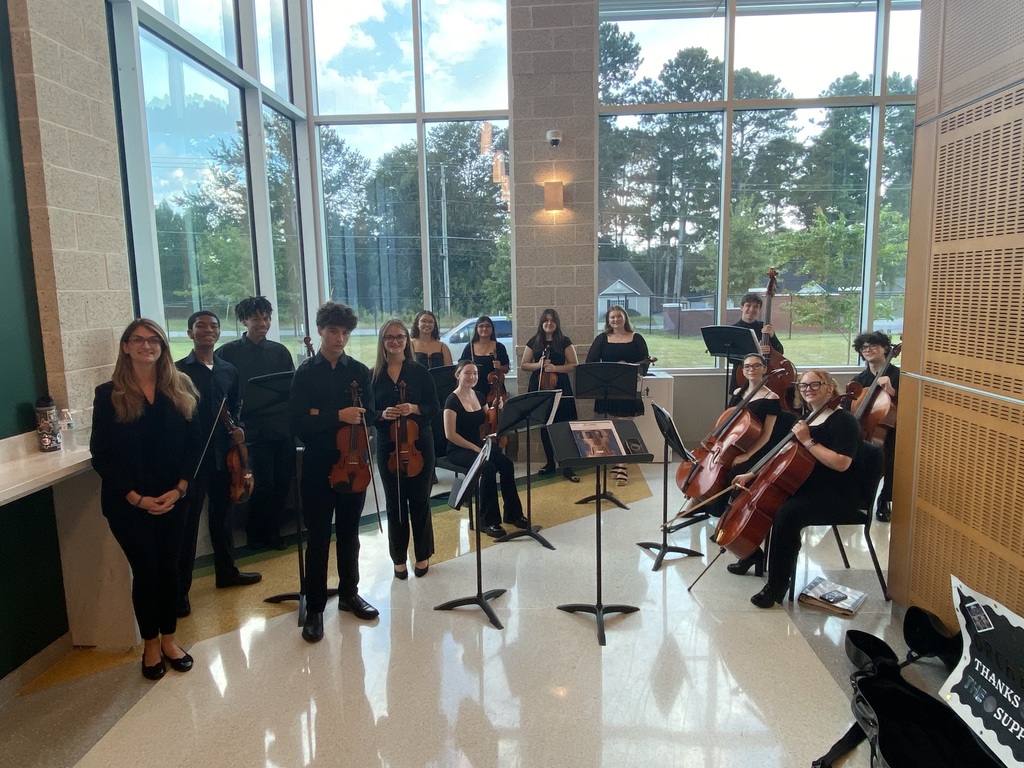Group of students posing in front of windows with string instruments.