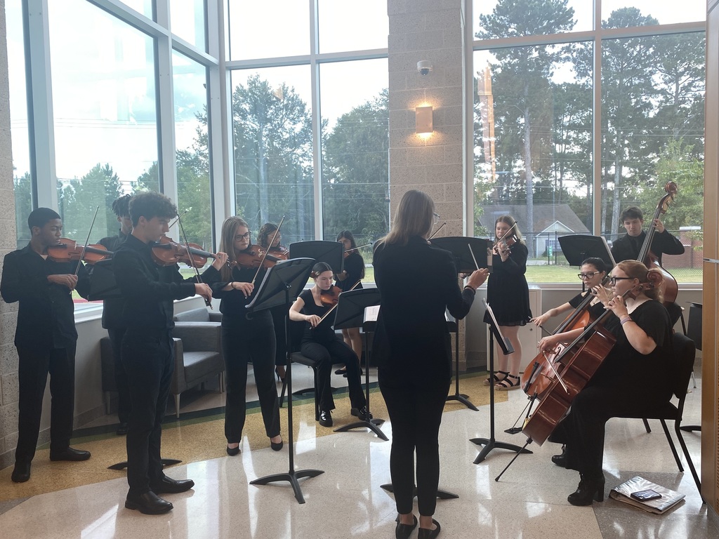 Group of musicians performing in front of glass windows with string instruments. 