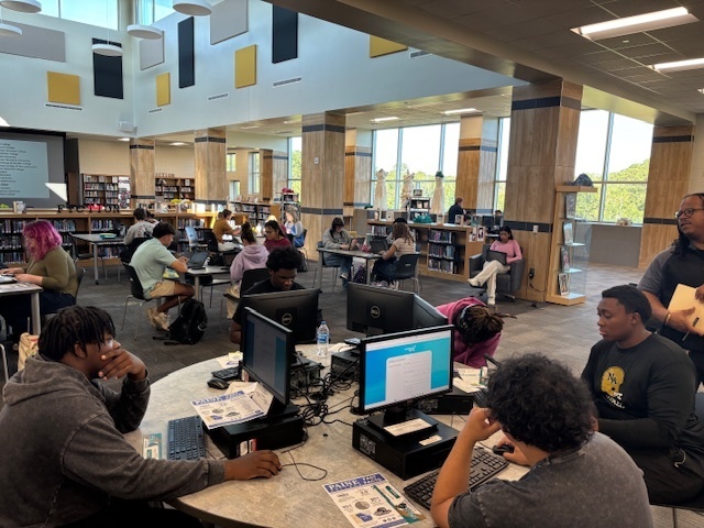 Students sitting around round desk at computers in library.