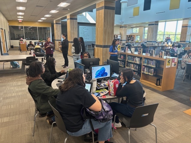 Students sitting around round desk at computers in library.