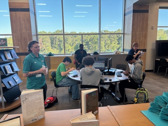Students sitting around round desk at computers in library.