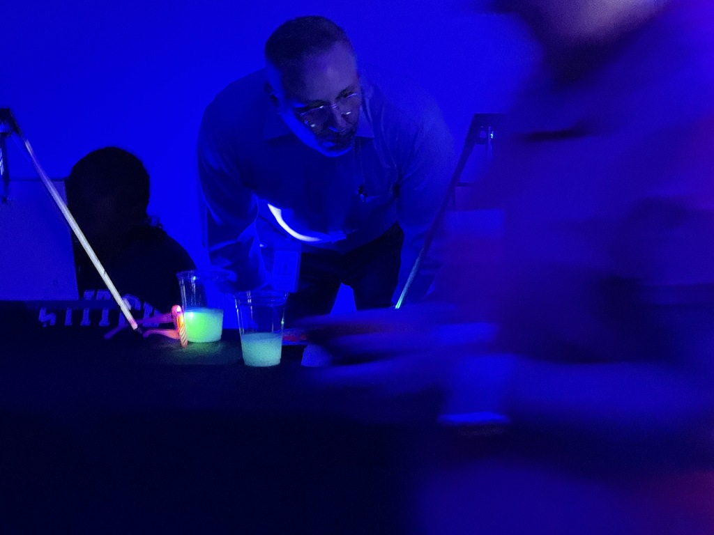 Adult male looks at students working on glow-in-the-dark paintings. 