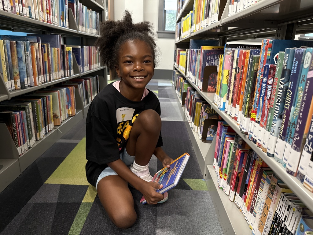 Student poses with library book at library. 